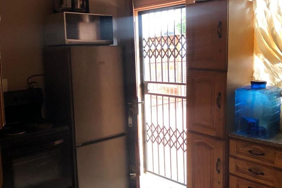 A compact kitchen featuring wooden cabinetry, tiled flooring, and a security gate leading to the exterior.