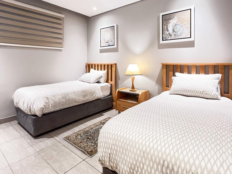 A well-maintained bedroom featuring neutral tiled flooring, recessed downlighting, and a modern roller blind.