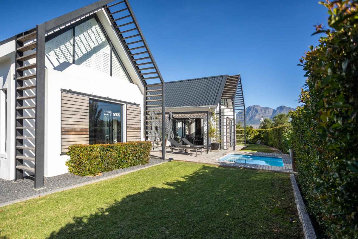 Modern rear exterior featuring a swimming pool, timber decking, and architectural steel framing set against a landscaped garden and mountain backdrop.
