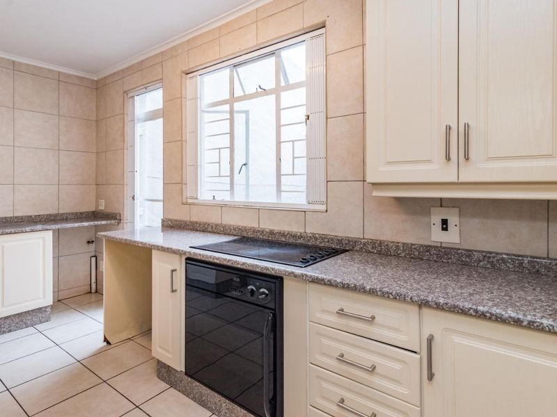 A functional kitchen featuring cream cabinetry, granite countertops, a built-in oven and hob, and neutral tiled finishes throughout.