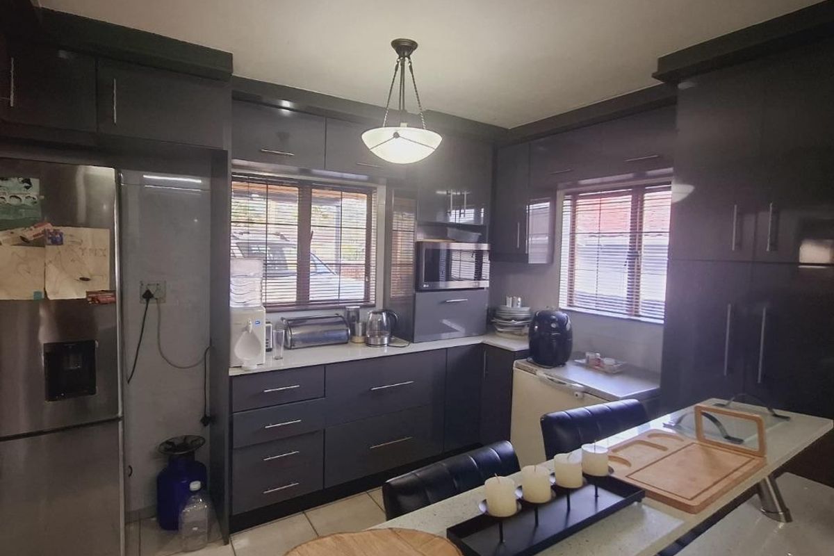 Modern kitchen featuring dark cabinetry, stone countertops, built-in microwave, and tiled flooring with ample natural light from dual windows.