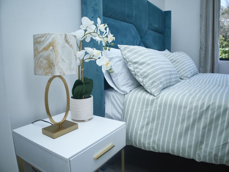 A well-lit bedroom featuring a blue upholstered headboard and a window with a view of the surrounding greenery.