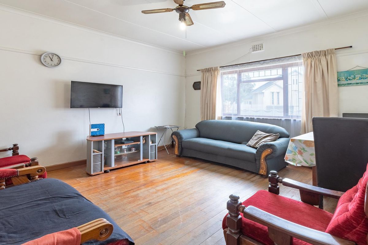 A spacious living room featuring original timber flooring, large windows with natural light, and a ceiling fan.