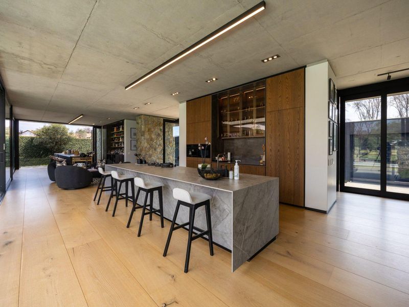 Modern open-plan living area featuring an exposed concrete ceiling, engineered wood floors, and a high-end stone kitchen island with integrated cabinetry.