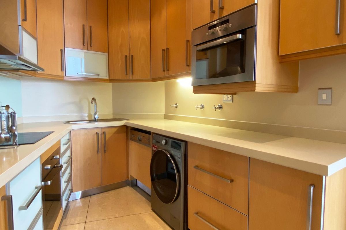 A functional kitchen featuring light wood cabinetry, stone countertops, a built-in oven, and integrated plumbing connections for laundry appliances.
