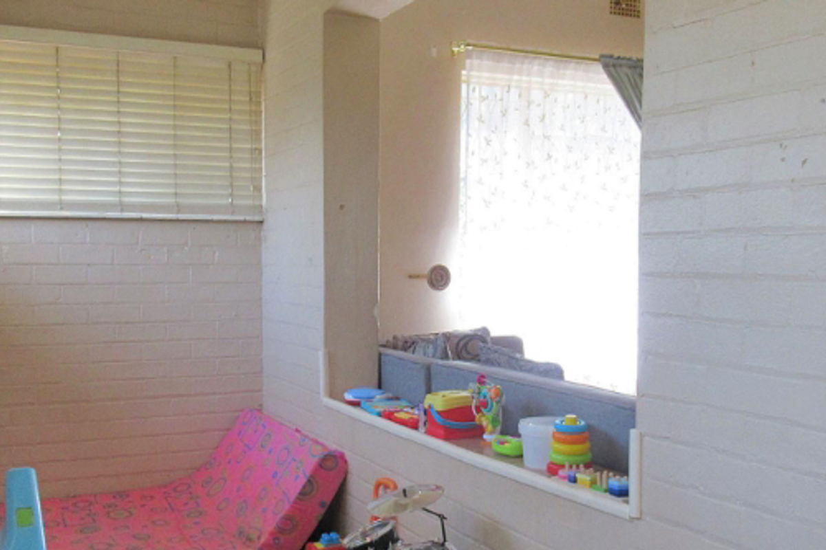 A multi-purpose room featuring painted brick walls, horizontal blinds, and a large interior window opening looking into the adjacent living space.