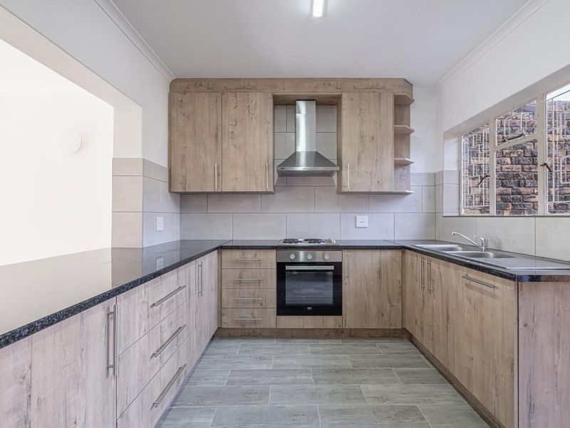 A clean, modern kitchen featuring wood-look cabinetry, granite countertops, built-in oven, gas hob, and a double sink with tiled backsplash.