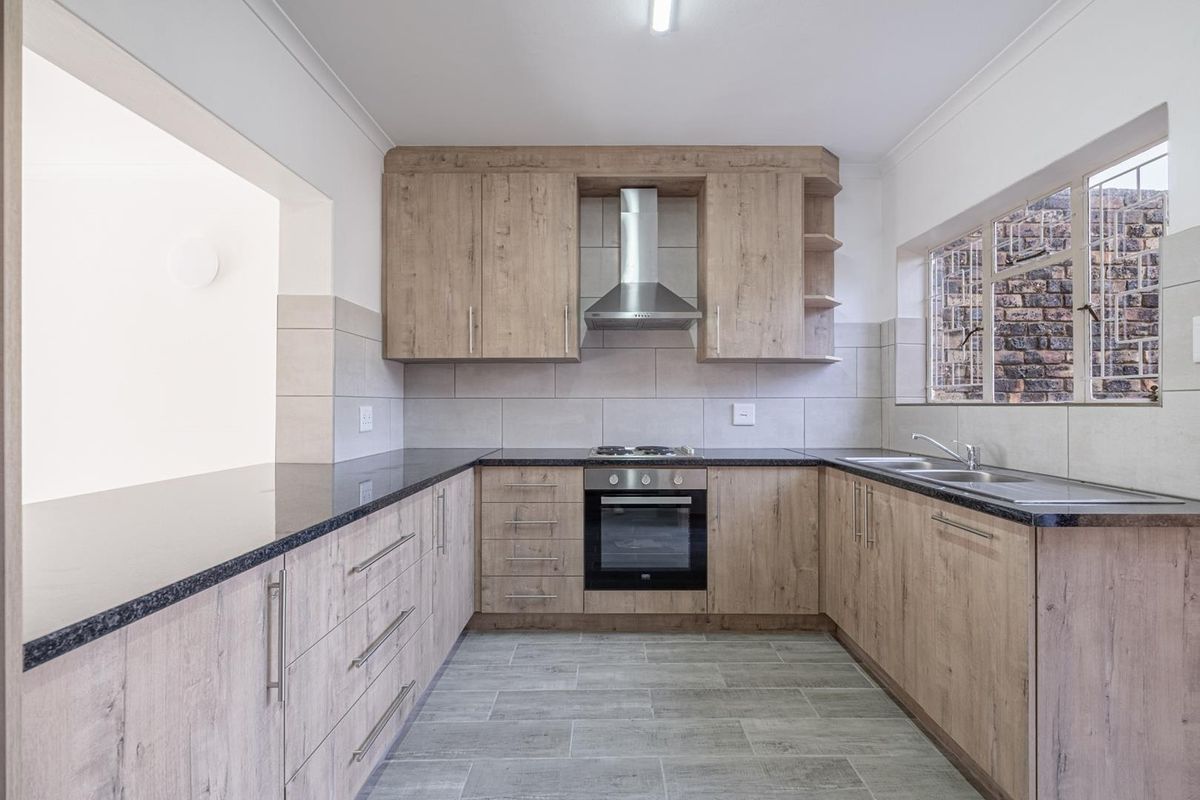 A clean, modern kitchen featuring wood-look cabinetry, granite countertops, built-in oven, gas hob, and a double sink with tiled backsplash.