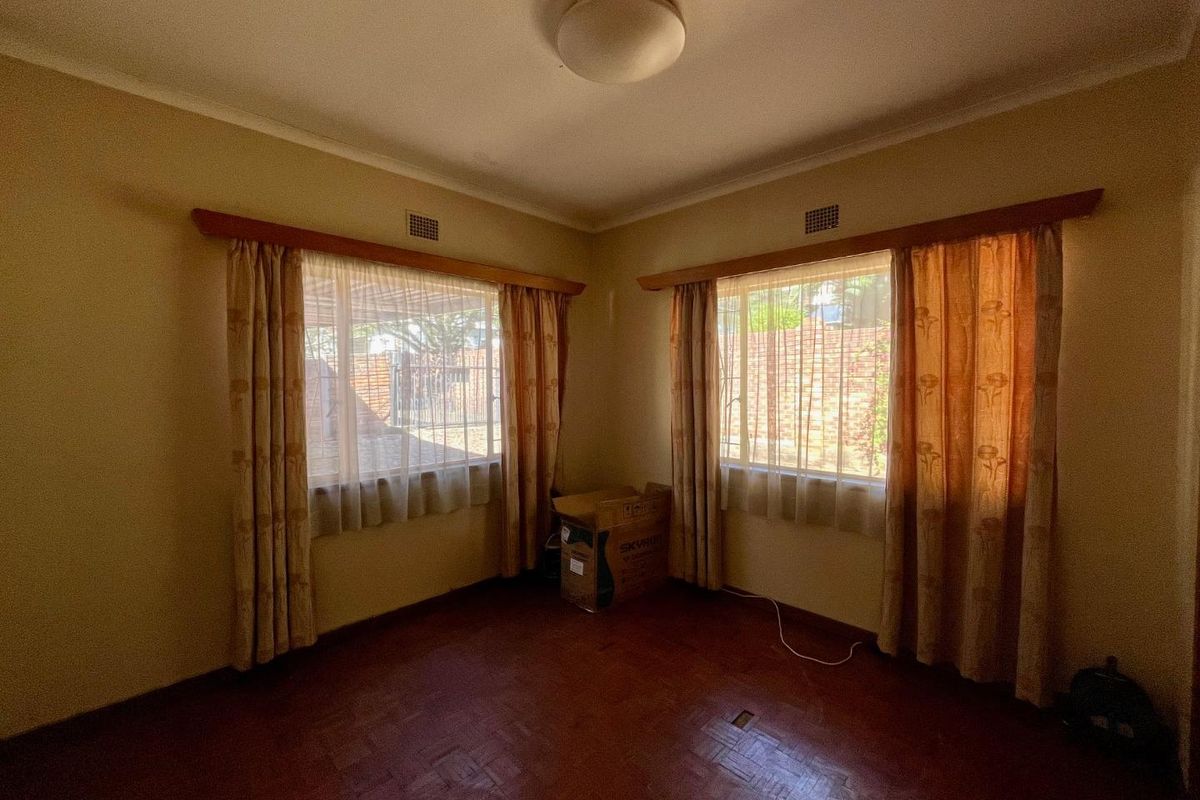 A bright, empty bedroom featuring original parquet flooring, dual aspect windows with curtain rails, and a central ceiling light fixture.