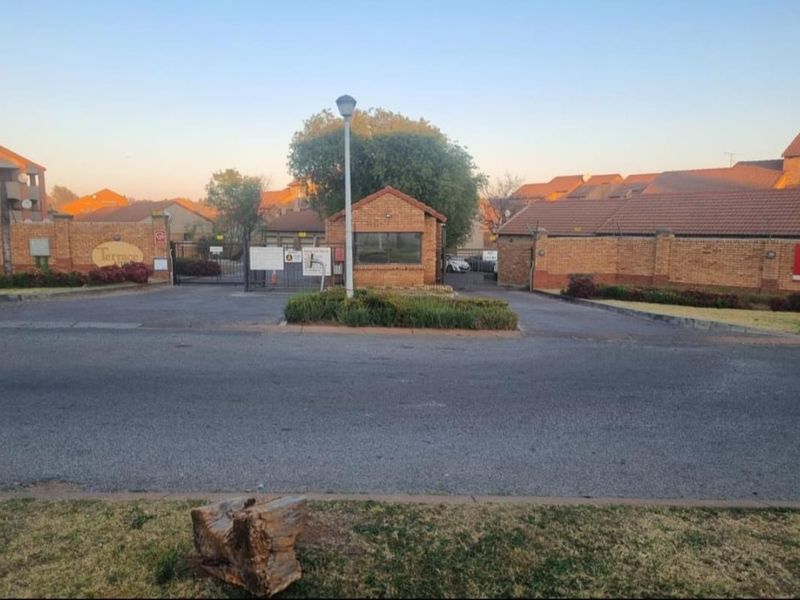 Street view of the apartment complex entrance featuring a brick perimeter wall, security gate, and guard house.