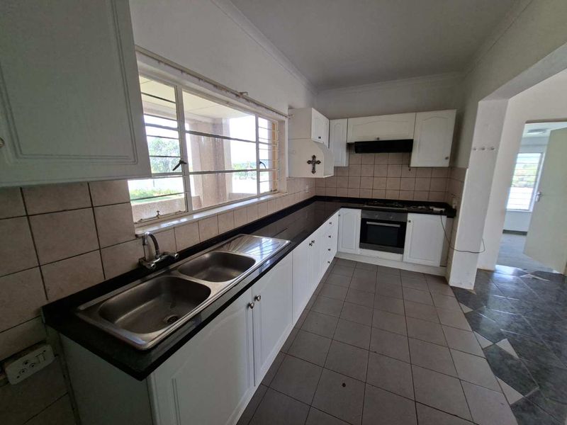 A functional kitchen featuring white cabinetry, black granite countertops, a double sink, and built-in cooking appliances with tiled finishes throughout.