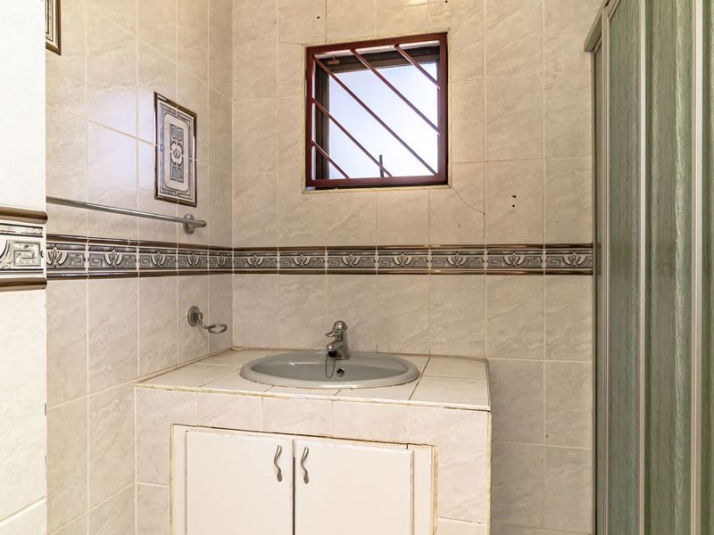 A dated bathroom featuring a built-in vanity with basin, tiled walls with decorative border, and a shower enclosure with security bars on the window.