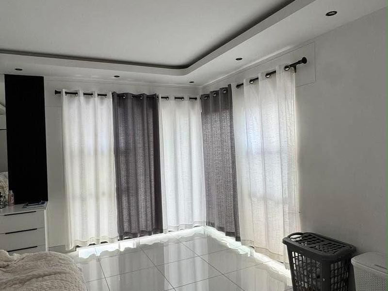 A bright bedroom featuring large windows with layered curtains, modern tiled flooring, and a recessed ceiling design with integrated lighting.