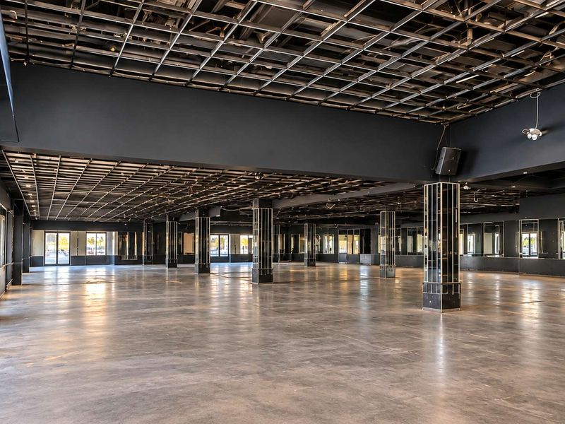 Expansive open-plan commercial space featuring polished concrete floors, exposed grid ceiling, and mirrored structural columns, offering a versatile layout for various business applications.