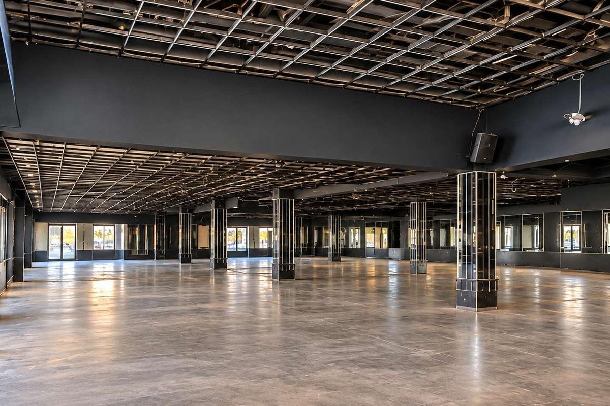 Expansive open-plan commercial space featuring polished concrete floors, exposed grid ceiling, and mirrored structural columns, offering a versatile layout for various business applications.