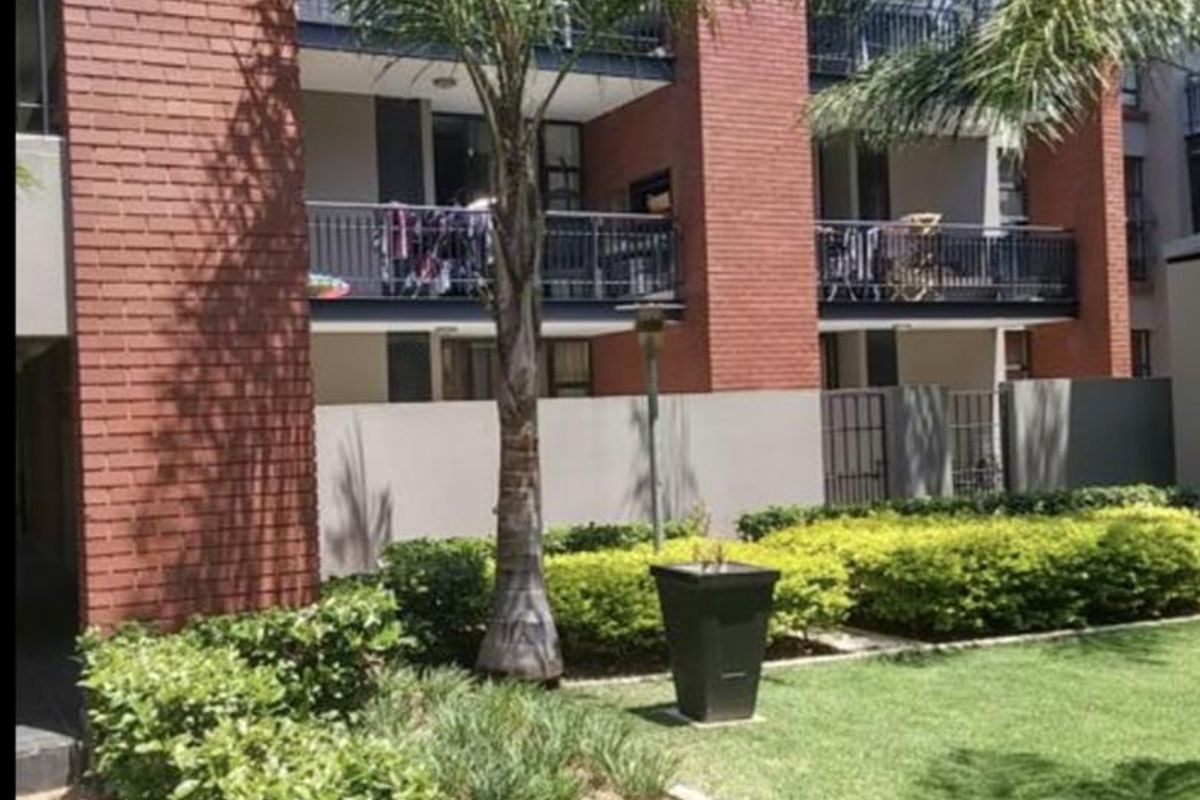 A view of the apartment complex rear facade featuring brick construction, private balconies with metal railings, and a well-maintained landscaped garden area.