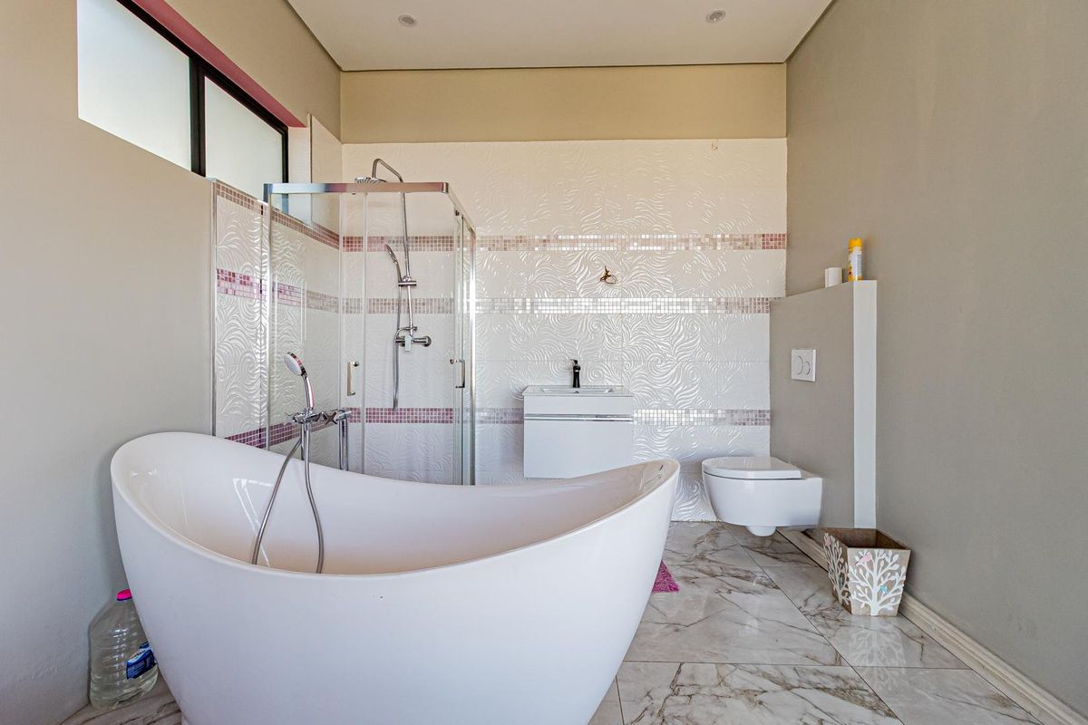 Modern bathroom featuring a freestanding soaking tub, glass-enclosed shower, wall-mounted vanity, and a concealed cistern toilet with decorative tiled feature walls.