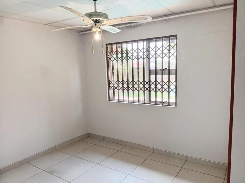 An empty bedroom featuring tiled flooring, a ceiling fan, and a window fitted with a security gate.