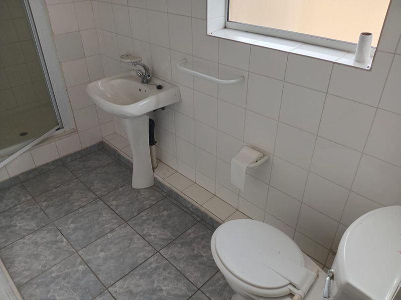 A functional bathroom featuring a pedestal basin, toilet, and shower enclosure with tiled finishes, requiring cosmetic updates to improve its overall condition.