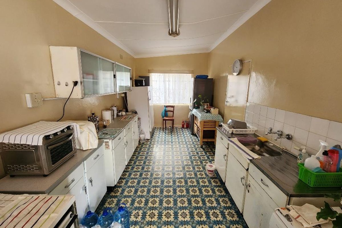 A dated kitchen featuring original cabinetry, patterned tile flooring, and a functional layout with a double sink and ample counter space.