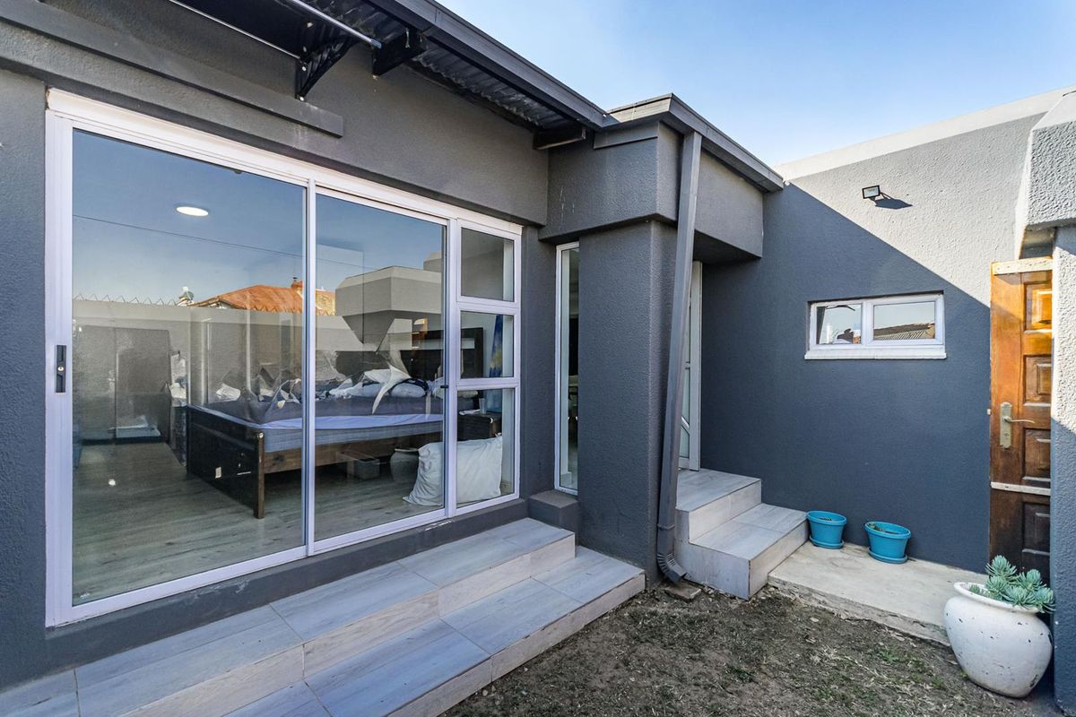 Rear exterior view featuring a modern dark grey facade, sliding glass doors, tiled entrance steps, and functional drainage downpipes.
