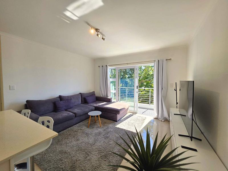 Bright living room featuring tiled floors, track lighting, and a sliding glass door leading to a balcony with natural light.