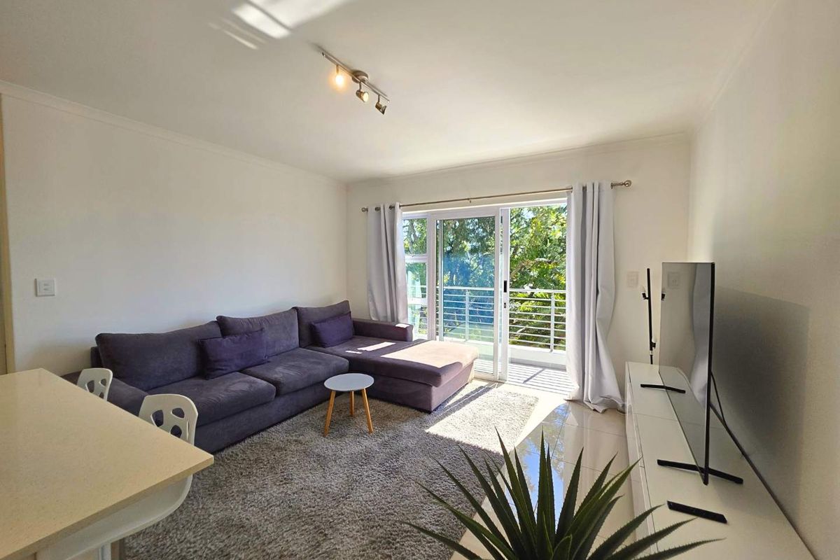 Bright living room featuring tiled floors, track lighting, and a sliding glass door leading to a balcony with natural light.