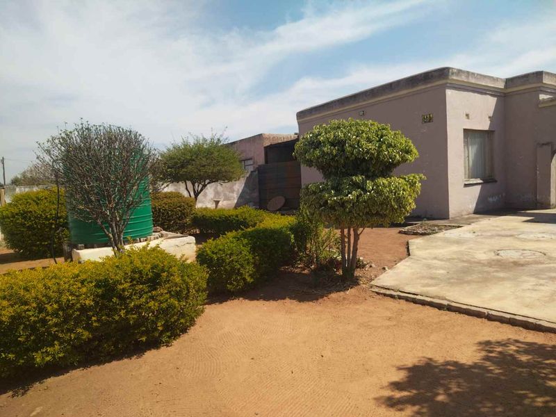 Rear exterior view of the property featuring a concrete patio area, established garden landscaping, and a water storage tank.