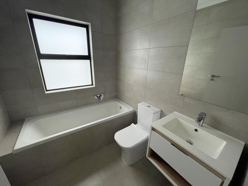 Modern bathroom featuring a built-in bathtub, wall-mounted toilet, and a contemporary vanity cabinet with an integrated basin and mirror.