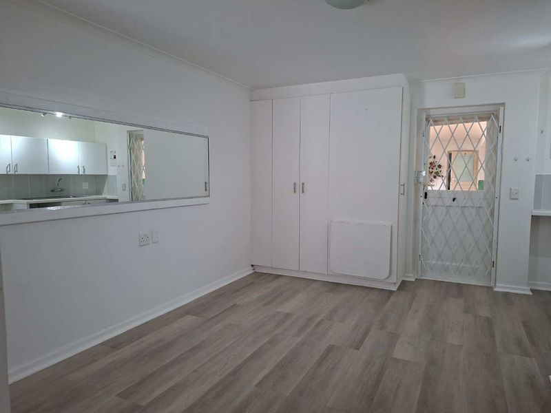 Open plan living area featuring modern laminate flooring, built-in storage cupboards, and a convenient pass-through window connecting to the kitchen space.