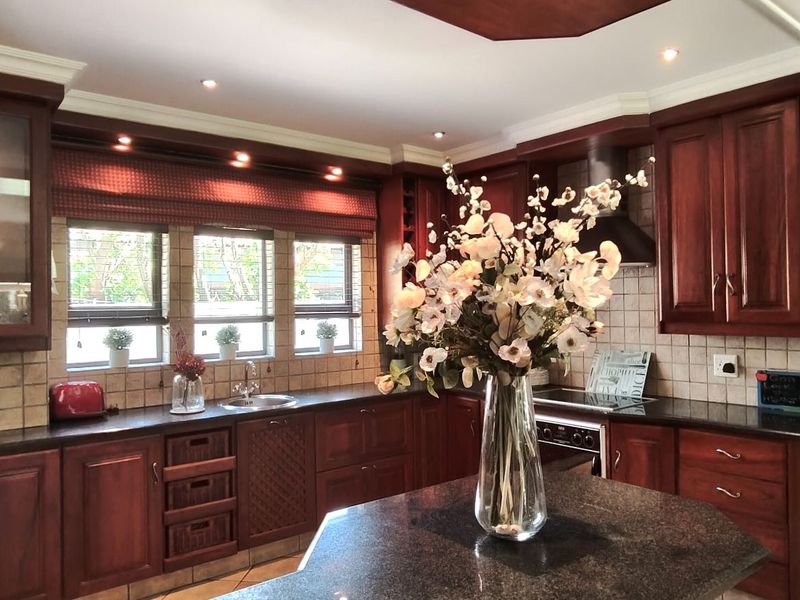 A well-maintained kitchen featuring dark wood cabinetry, granite countertops, a tiled backsplash, and integrated appliances with recessed lighting.