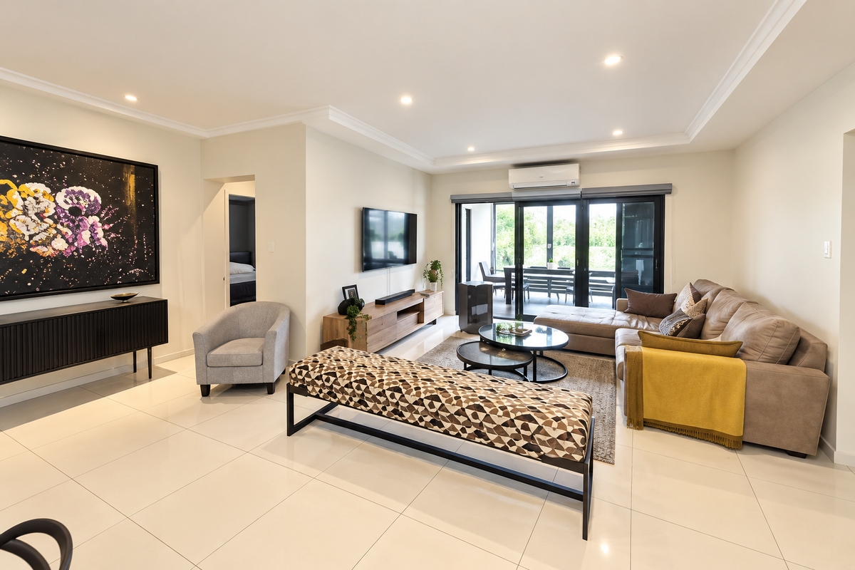 A bright and modern living room featuring polished porcelain floor tiles, recessed downlighting, and large sliding glass doors leading to an outdoor patio area.