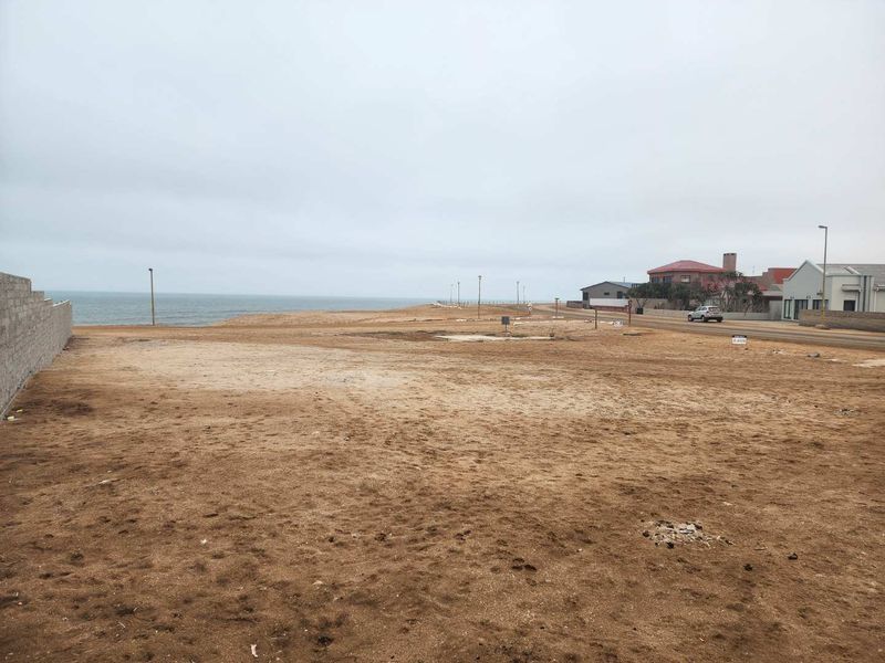 A vacant residential plot situated in a coastal area, featuring a boundary wall and direct access to the street with ocean views.