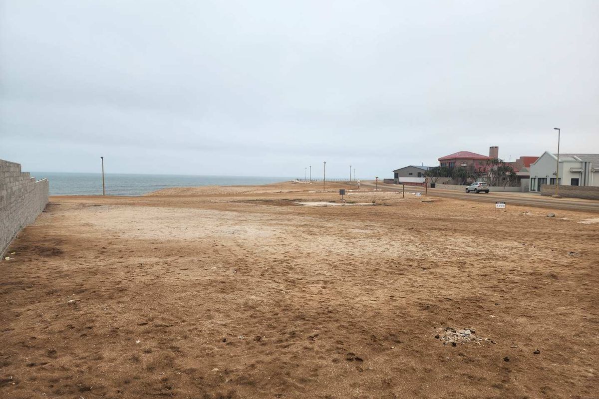A vacant residential plot situated in a coastal area, featuring a boundary wall and direct access to the street with ocean views.