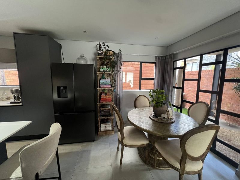Modern open-plan living and dining area featuring sleek dark cabinetry, large black-framed windows, and neutral tiled flooring, creating a bright and contemporary atmosphere.