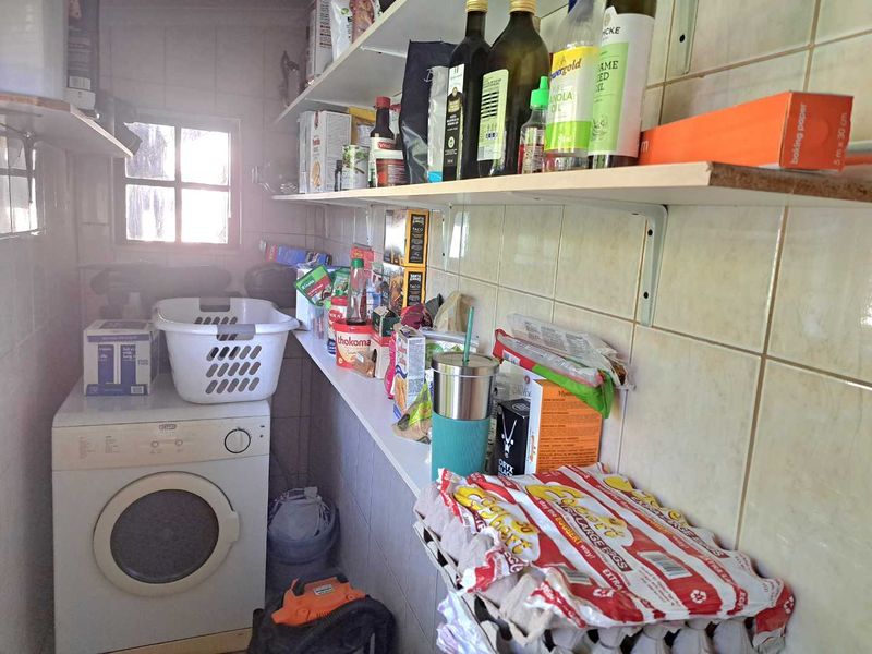 A functional scullery or laundry area featuring tiled walls, wall-mounted shelving for storage, and a dedicated space for a washing machine.