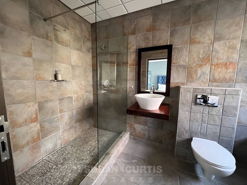 Modern bathroom featuring a walk-in shower with pebble flooring, wall-mounted basin, and a concealed cistern toilet with full-height stone-look wall tiling.