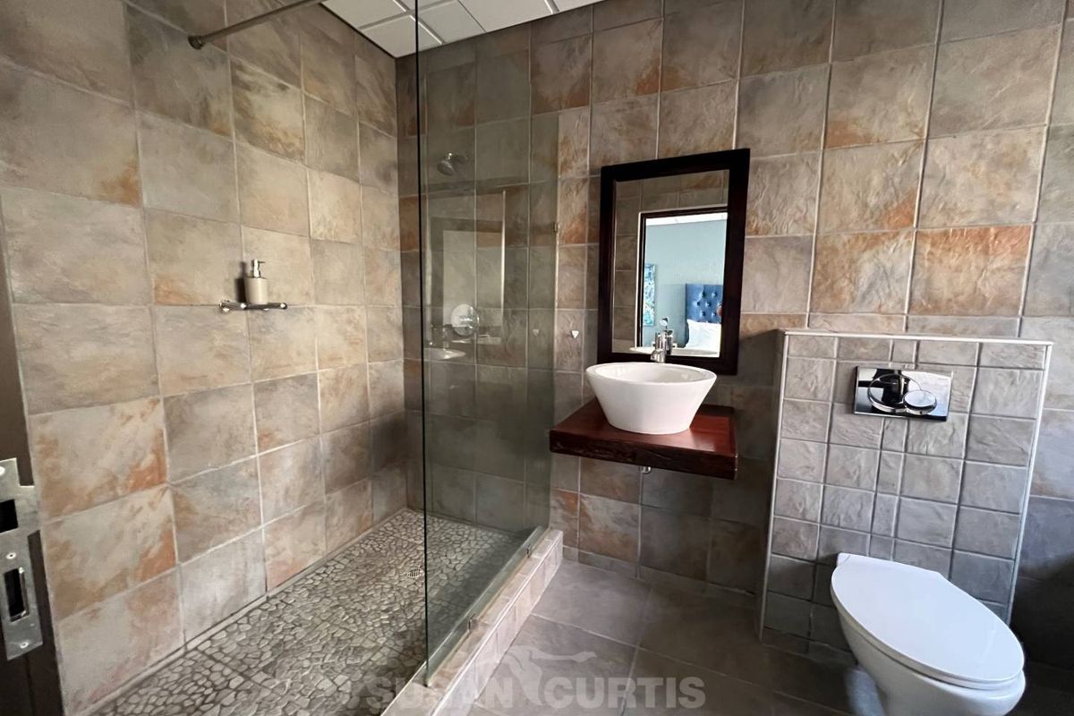 Modern bathroom featuring a walk-in shower with pebble flooring, wall-mounted basin, and a concealed cistern toilet with full-height stone-look wall tiling.