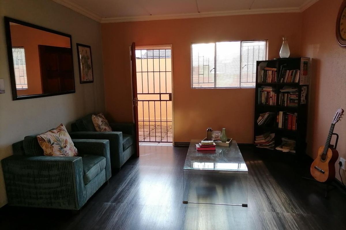 A living room featuring dark laminate flooring, warm-toned walls, and a security gate leading to an outdoor area.