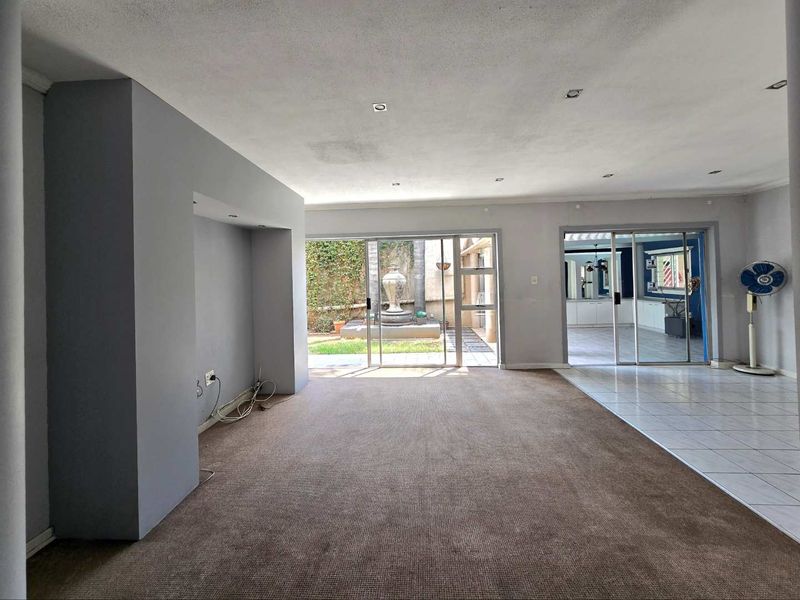 Spacious open-plan living area featuring a built-in media wall, recessed lighting, and sliding glass doors leading to an outdoor patio area.