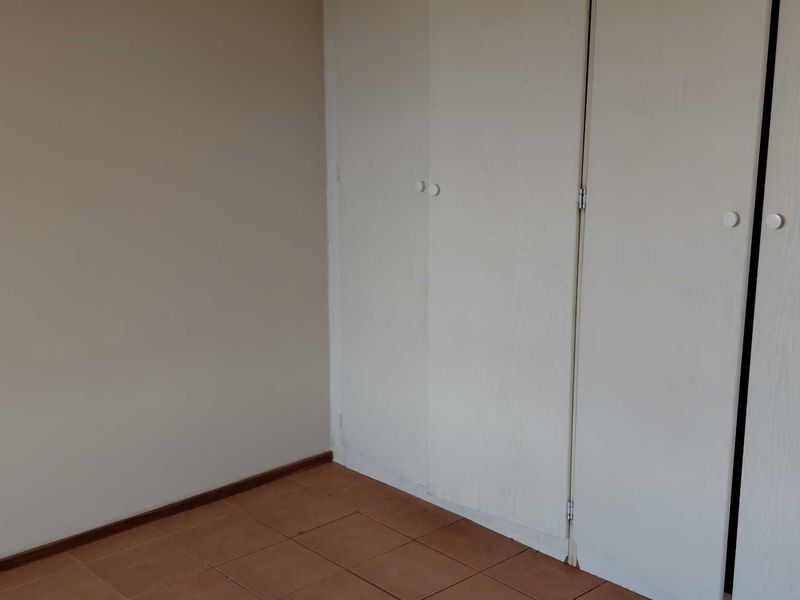 An empty bedroom featuring tiled flooring and built-in cupboards with white doors.