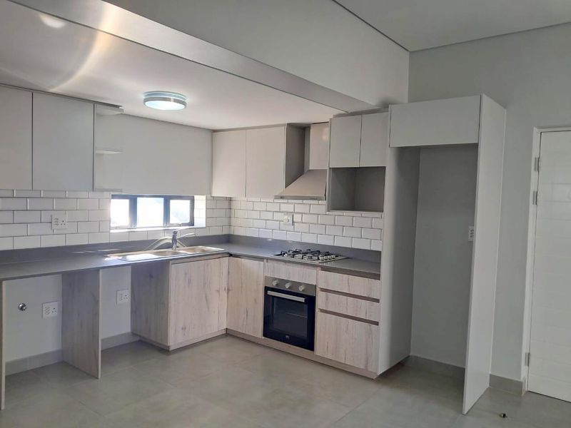 Modern kitchen featuring light wood-finish cabinetry, subway tile backsplash, stone countertops, integrated gas hob, oven, and extractor fan in a clean, empty space.