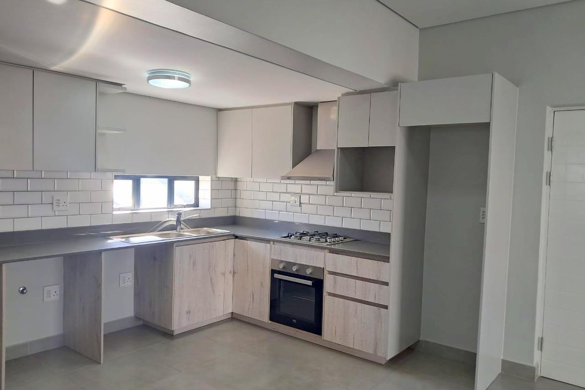 Modern kitchen featuring light wood-finish cabinetry, subway tile backsplash, stone countertops, integrated gas hob, oven, and extractor fan in a clean, empty space.