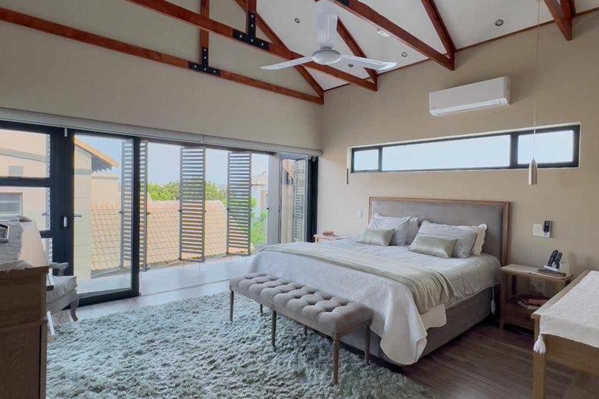 Spacious bedroom featuring high vaulted ceilings with exposed timber trusses, wood-look flooring, split-system air conditioning, and large sliding doors opening to a private balcony.