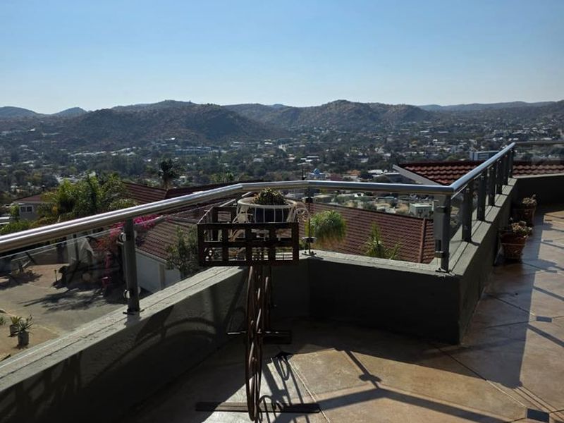 Spacious balcony featuring a modern stainless steel and glass balustrade, tiled flooring, and expansive panoramic views of the surrounding landscape.