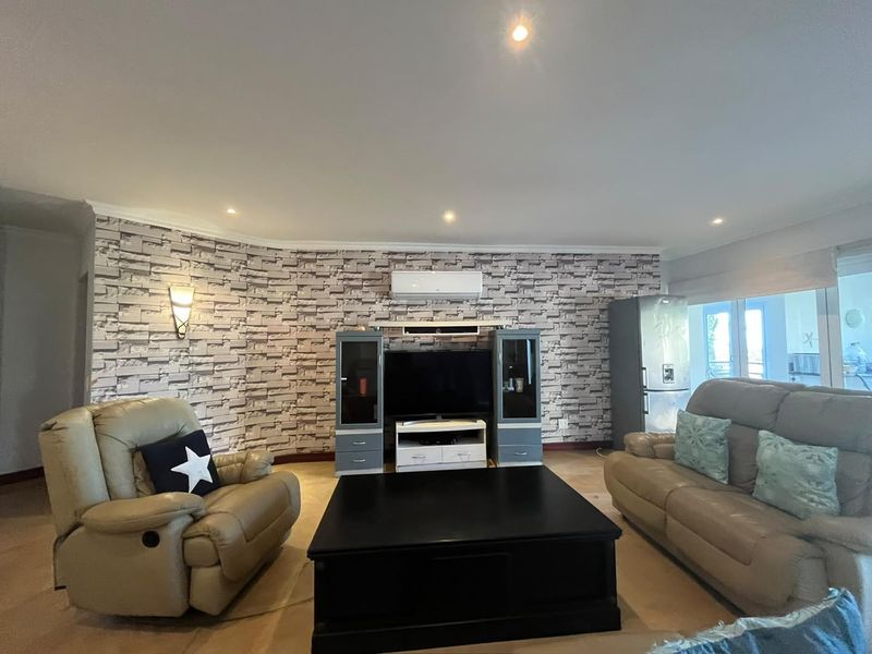 A living room featuring a textured brick-effect feature wall, recessed downlighting, and a wall-mounted split-system air conditioning unit.