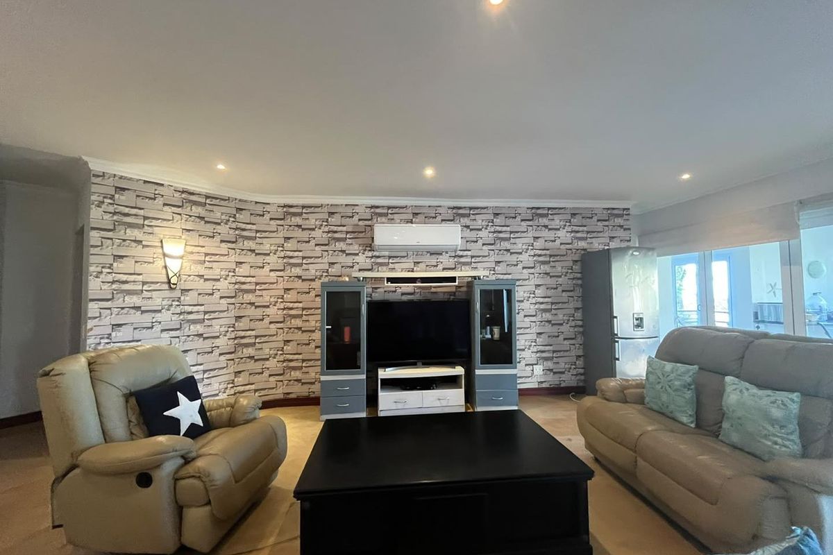 A living room featuring a textured brick-effect feature wall, recessed downlighting, and a wall-mounted split-system air conditioning unit.