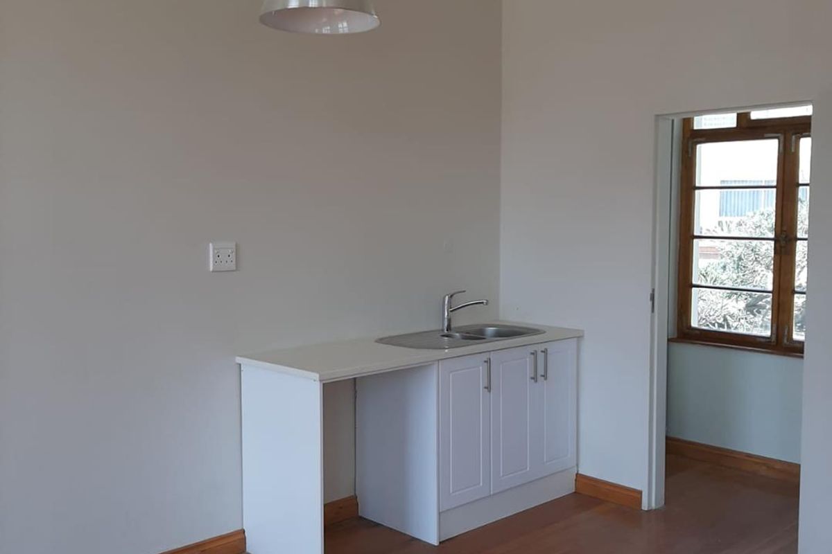 A compact kitchenette area featuring a white base cabinet, stainless steel sink, and a pendant light fixture, set against polished wooden flooring.