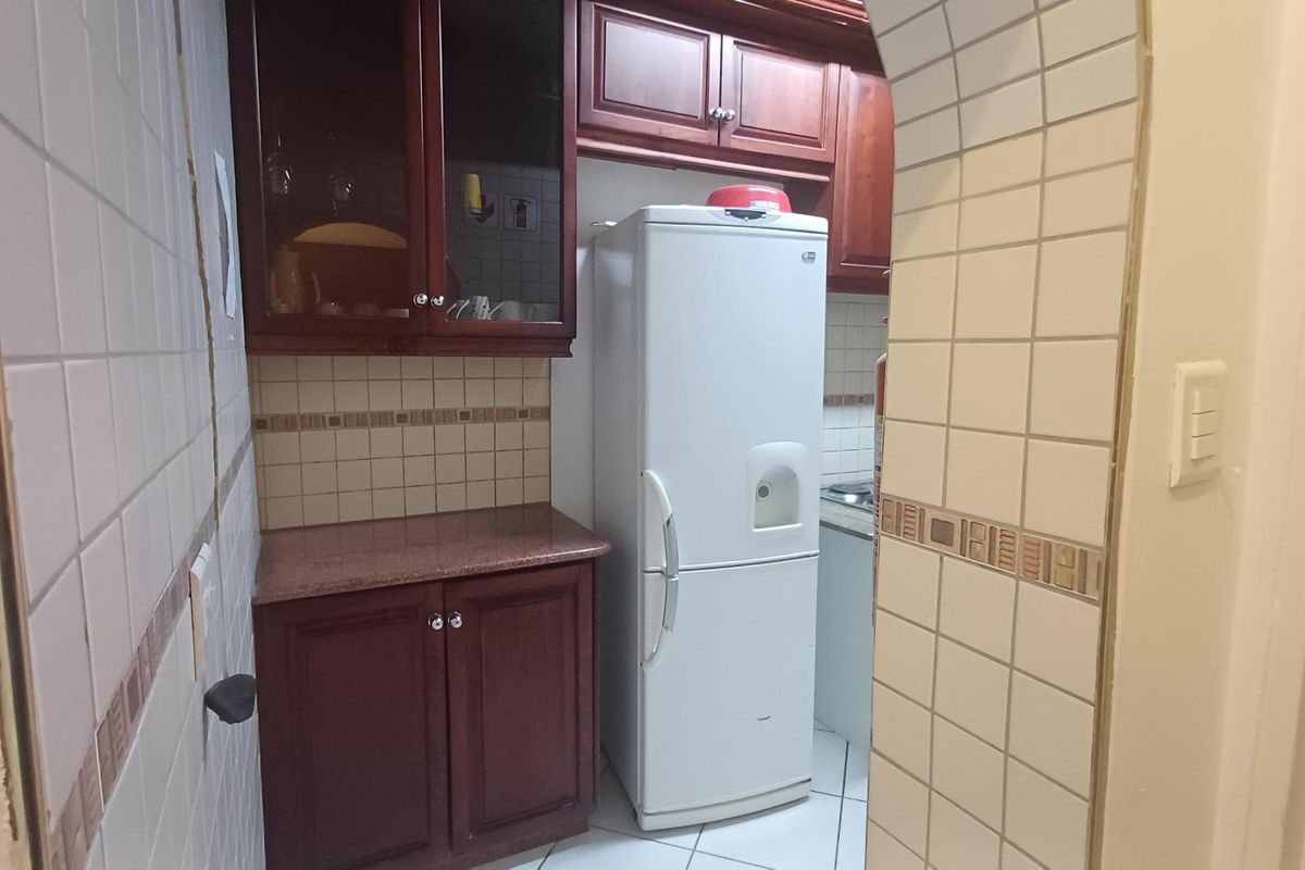 A compact kitchen area featuring dark wood cabinetry, tiled walls with decorative accents, and tiled flooring.