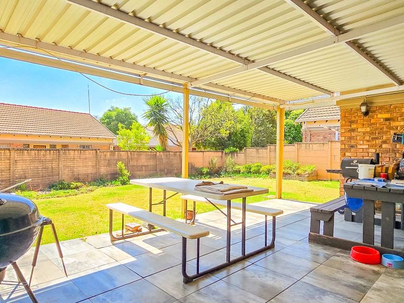 A covered outdoor patio area featuring tiled flooring and exposed brickwork, overlooking a private garden space.